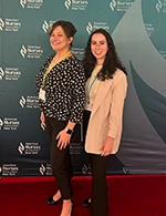 Two woman smiling in front of conference backdrop.