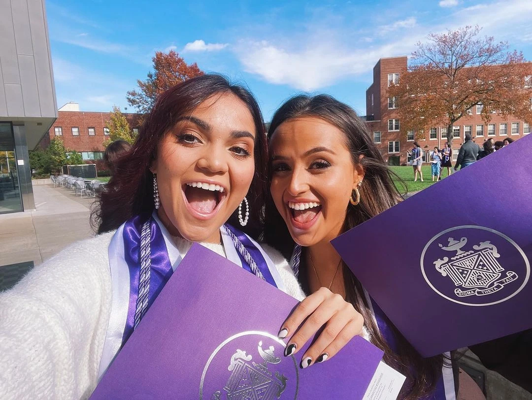 Two women smiling and holding Sigma Theta Tau purple folders.